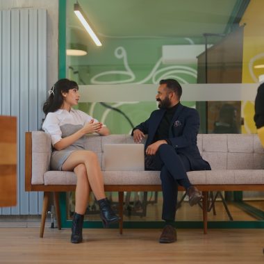 Two multi-ethnic a businessman and a businesswoman are working together and talking while using a laptop in a modern co-working office space.